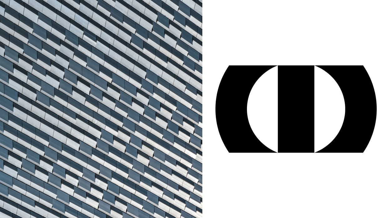 The image shows a close-up of a modern building facade composed of staggered horizontal panels in shades of blue and gray. The panels create a diagonal, rhythmic pattern across the surface, emphasizing repetition and depth. On the right side, a bold black geometric symbol with circular and rectangular shapes appears on a white background. The overall composition contrasts architectural texture with minimal graphic design.